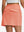 Back lower body shot of model wearing peach pink women's stretch a-line golf skort with 7 pockets