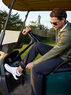 Model seated in golf cart, adjusting pant leg, wearing water-resistant fleece lined pants in black
